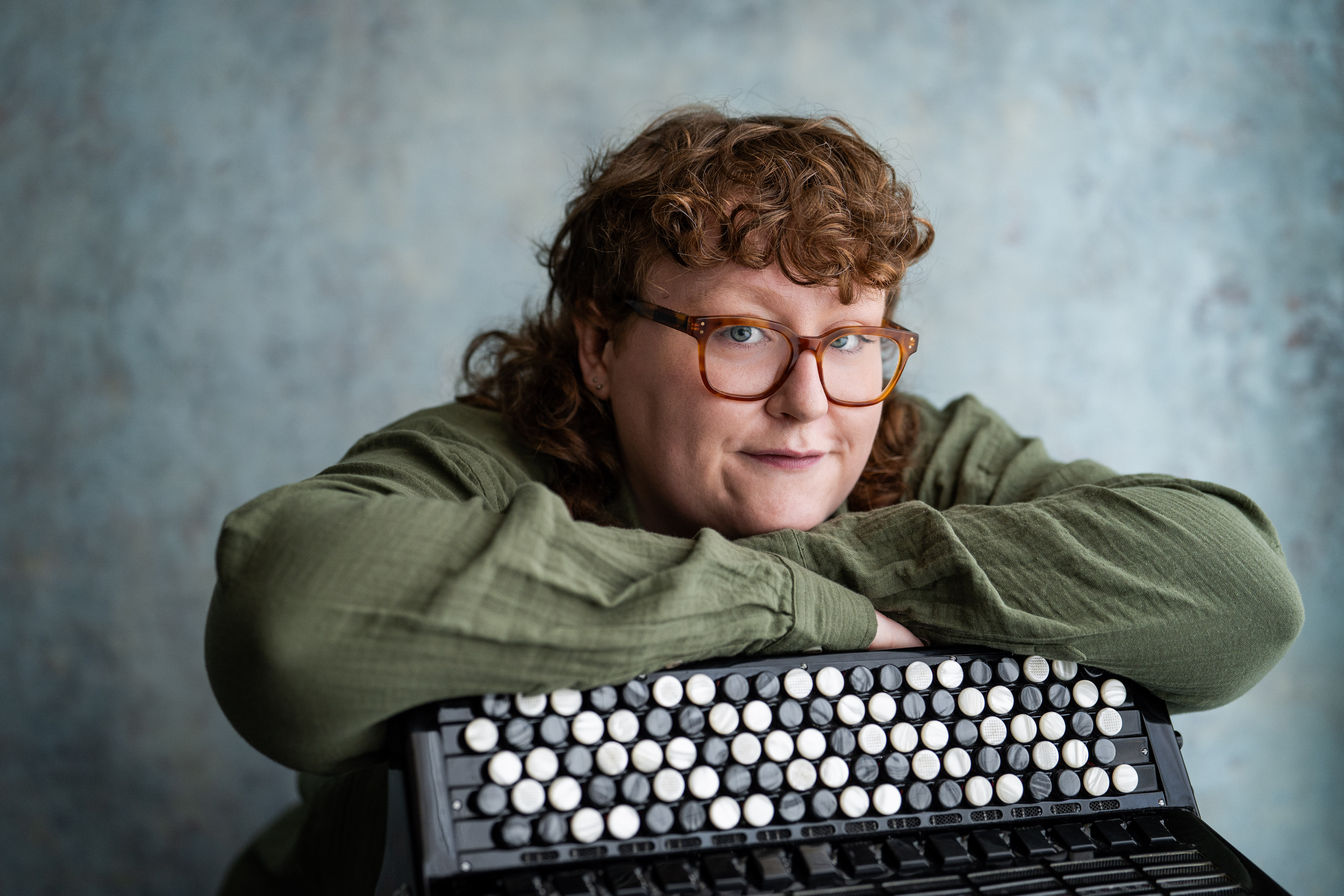 London-based accordionist Aine McLoughlin in a green shirt leaning on an accordion.